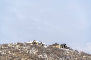 Çimenli tepenin tepesine inşa edilmiş evler bulutlu kış gökyüzüne karşı karla kaplı.