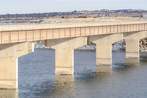 Pont massif sur lac brillant avec fond de paysage herbeux et neigeux — Photo