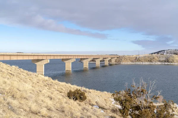 寒い冬の日に青い湖の上の橋を見下ろす草の山 — ストック写真
