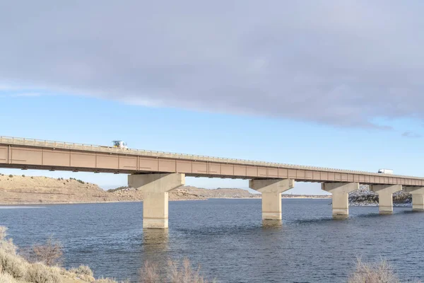 Bridge across a lake with scenic view of hills and cloudy blue sky in winter — 스톡 사진