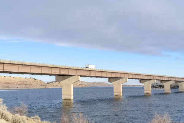 Truck on a stringer bridge acroos blue lake overlooking hills and cloudy sky — 스톡 사진