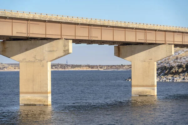 Fokus auf eine Balkenbrücke, die von Widerlagern über dem blauen See gegen bewölkten Himmel gestützt wird — Stockfoto