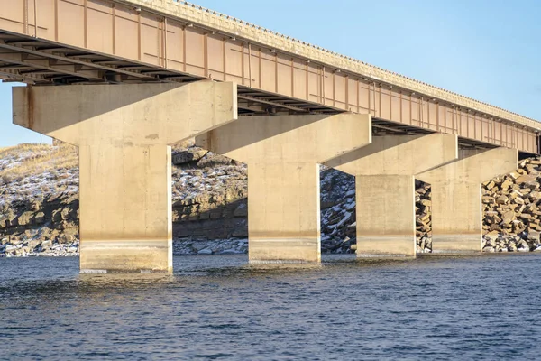 Massive Widerlager, die die Spannweite einer Balkenbrücke über blaues Seewasser stützen — Stockfoto