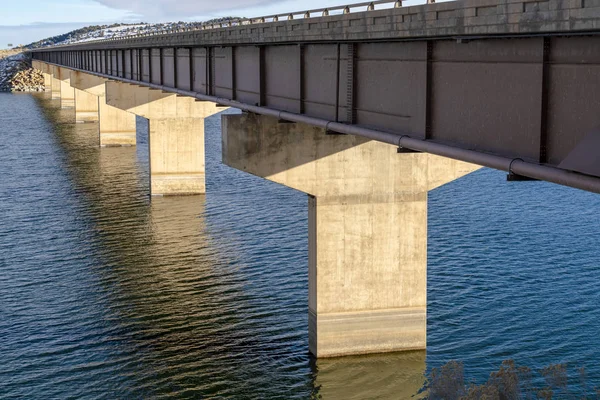 Dek van een balkenbrug die wordt ondersteund door balustrades of pijlers die over blauw water lopen — Stockfoto