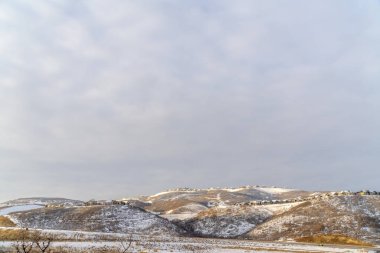 Karla kaplı tepelerde yuva yapmış evleri olan güzel doğal bir manzara.