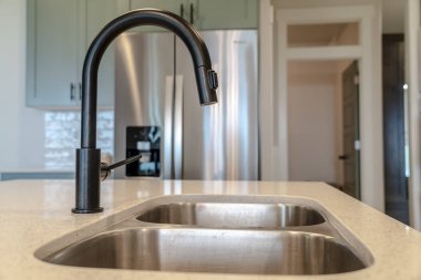 Mutfak lavabosunun altında çift lavabo ve buzdolabına karşı siyah musluk.