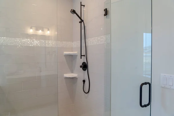 Black shower fixtures of a bathroom with white tile wall and clear glass door