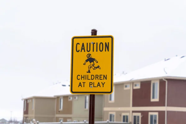 Gelbe Warnung Kinder beim Spielschild vor verschwommenem Gebäude und bewölktem Himmel — Stockfoto