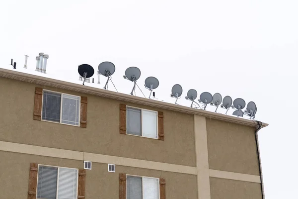 Antenas en forma de cuenco montadas en el techo nevado del edificio residencial en invierno —  Fotos de Stock