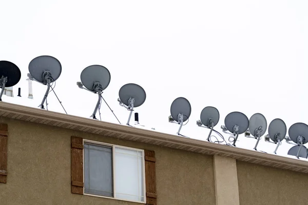 Antenas parabólicas instaladas no telhado do edifício residencial com neve no inverno — Fotografia de Stock