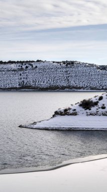 Dikey kare güneşli kış günü soğuk sakin göl ve tepeler beyaz karla örtülü.