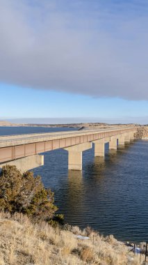 Güneşli bir kış gününde karla kaplı tepeleri birbirine bağlayan göl üzerindeki dikey köprü.