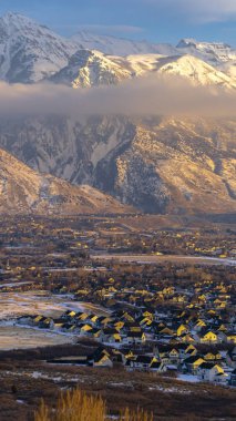 Dikey çerçeve Karlı Timpanogos Dağı ve büyüleyici evler bulutlu mavi gökyüzüne karşı gün batımında