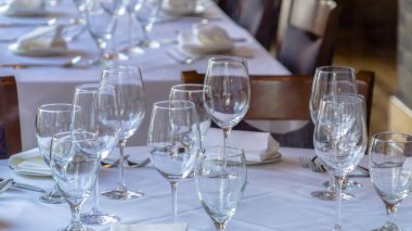 Fotoğraf Panorama Şarap kadehleri çatal kaşıklar tabak ve peçeteler beyaz kumaşlı bir masanın üzerinde.