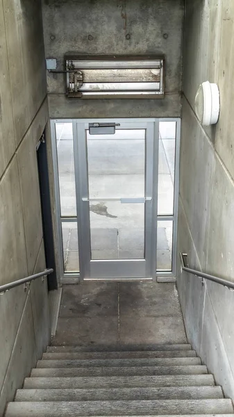 Rama pionowa Schody wewnątrz budynku schodzącego do szklanych drzwi prowadzących na zewnątrz — Zdjęcie stockowe