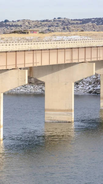 Vertical frame Massive bridge over shiny lake with grassy and snowy landscape background — 스톡 사진