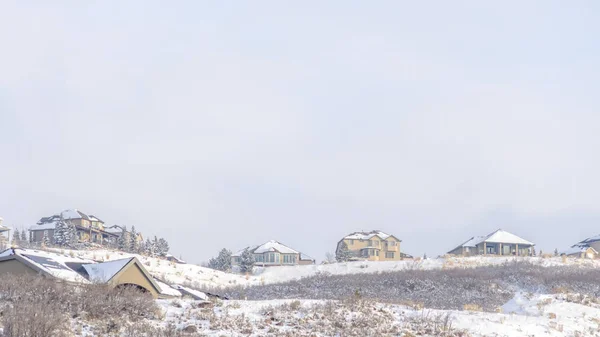 Foto Panorama Sneeuw bedekt heuveltop met besneeuwde huizen tegen uitgestrekte bewolkte lucht in de winter — Stockfoto