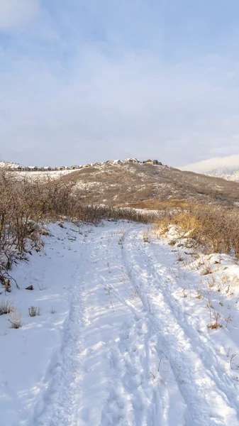 Marco vertical Camino en la colina con nieve con vistas a las casas y la montaña contra el cielo nublado — Foto de Stock