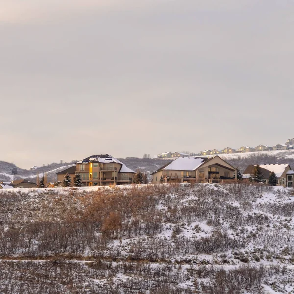 Marco cuadrado Casas en colinas cubiertas de hierba y nieve contra el cielo nublado en un día de invierno helado — Foto de Stock