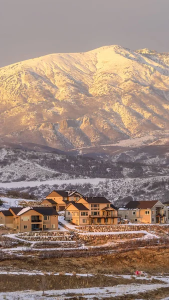 Foto Marco vertical Casas en terreno residencial montañoso espolvoreado con nieve fresca de invierno al atardecer —  Fotos de Stock