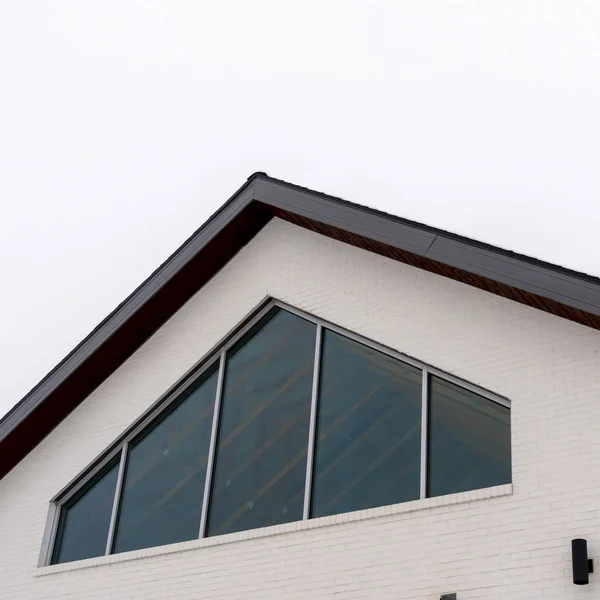 Foto Marco cuadrado Exterior del hogar con ventana tringular y pared blanca bajo techo a dos aguas — Foto de Stock