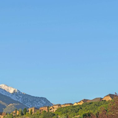 Kare çerçeveli evler açık mavi gökyüzü ve arka planda karlı dağ manzaralı bir tepede
