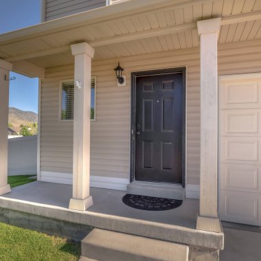 Kare çerçeveli ev cephesi beton verandalı ve garaj kapısının yanındaki ön kapılı.