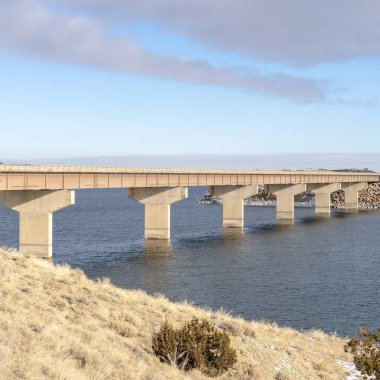 Soğuk bir kış gününde, mavi gölün üzerindeki köprüye bakan Kare Grassy Dağı
