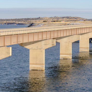 Sakin göl üzerinde uzanan Stringer Köprüsü karlı arazi ve bulutlu gökyüzü manzaralı