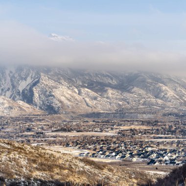 Banliyödeki kare çerçeveli evler karla kaplı çarpıcı dağ manzaralarıyla çevrili.