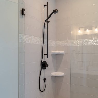 Fotoğraf kare çerçeve, beyaz fayans duvarlı ve cam kapılı bir banyonun siyah duş armatürleri.