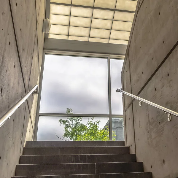 Square frame Stairs between interior walls of building leading to glass wall with sky view