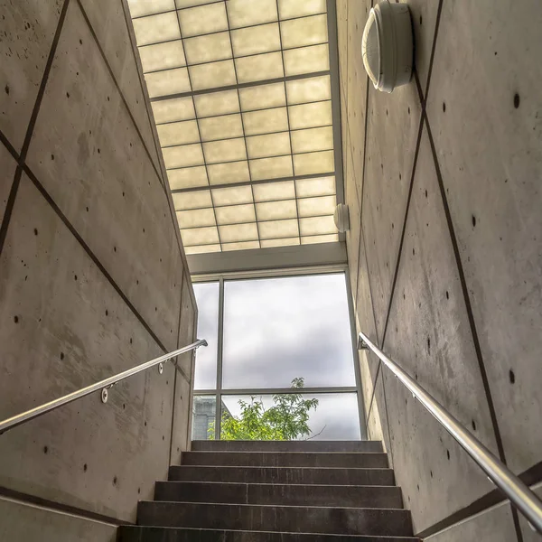 Square Stairs between interior walls of building leading to glass wall with sky view