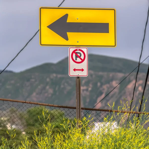 Square frame No Parking On Both Sides and directional arrow signs against fence and plants — Stock Photo, Image