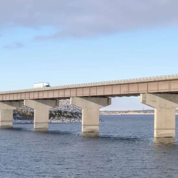 Vierkante brug over een meer met prachtig uitzicht op heuvels en bewolkte blauwe lucht in de winter — Stockfoto