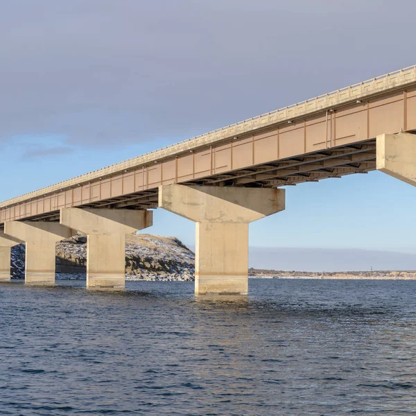 Quadratische Stringerbrücke über einen See mit Blick auf verschneites Gelände und bewölkten Himmel — Stockfoto