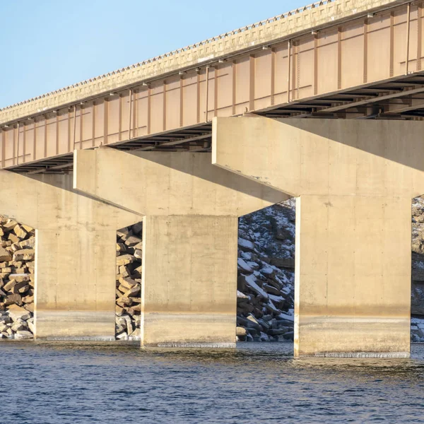 Vierkante Massieve abutments ondersteunen de spanwijdte van een balkenbrug over blauw meerwater — Stockfoto