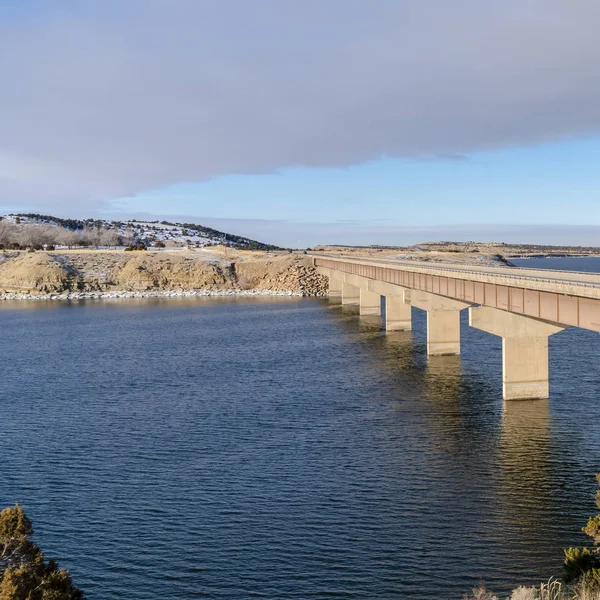 Quadratische Brücke über den See verbindet schneebedeckte Hügel an einem sonnigen Wintertag — Stockfoto