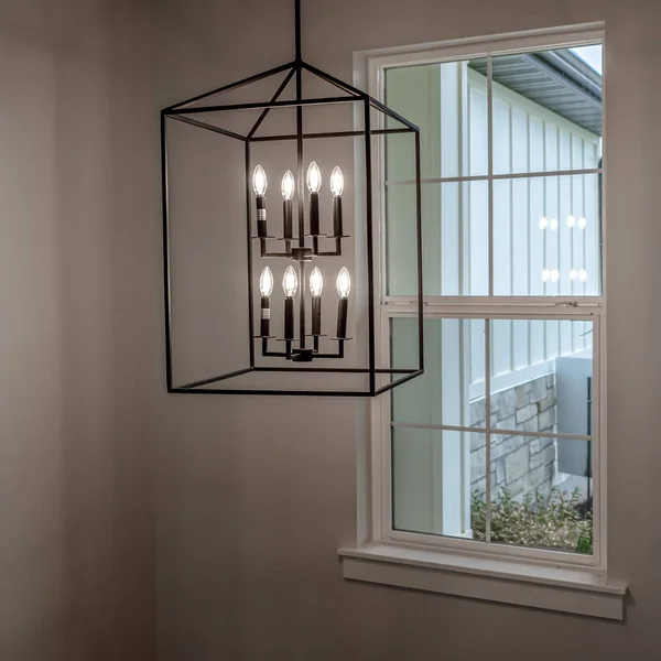 Quadratischer Rahmen geometrischer Kronleuchter, der von der Decke des Hauses gegen Fenster und Wand hängt — Stockfoto