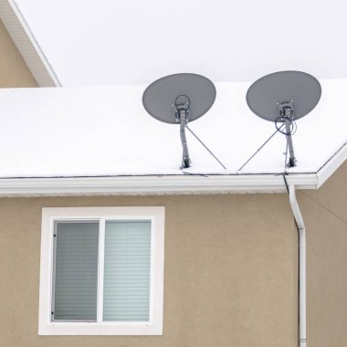 Fotoğraf Meydanı çerçeveli uydu çanakları kışın karla kaplı evin çatısında.