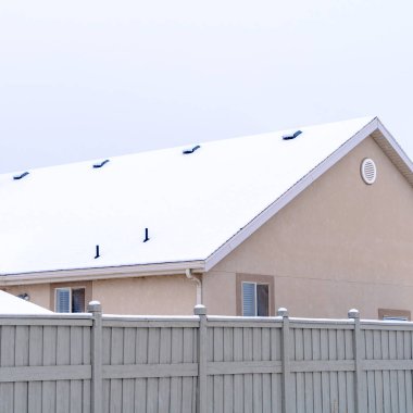 Square Home exterior with gable roof blanketed with snow against cloudy sky in winter clipart