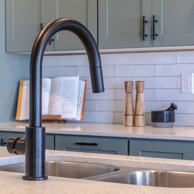 Kare çerçeveli mutfak adası lavabosu ve mutfak dolapları ve aletlerine karşı siyah musluk