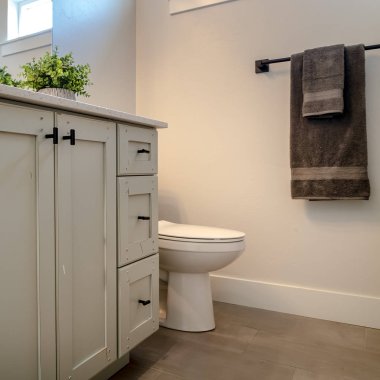 Kare tuvalet ve makyaj dolabı. Banyonun içinde beyaz duvar, kahverengi zemin ve pencereli.