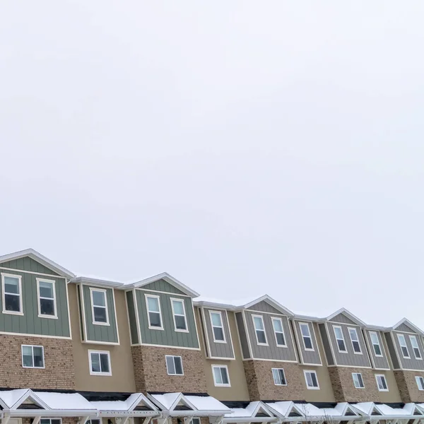 Quadratische Außenfassade von Reihenhäusern mit Satteldächern und Ziegelmauer gegen bewölkten Himmel — Stockfoto