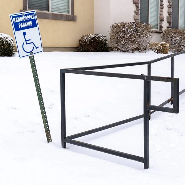 Square Handicapped Parking sign and wheelchair ramp at a snowy parking lot in winter