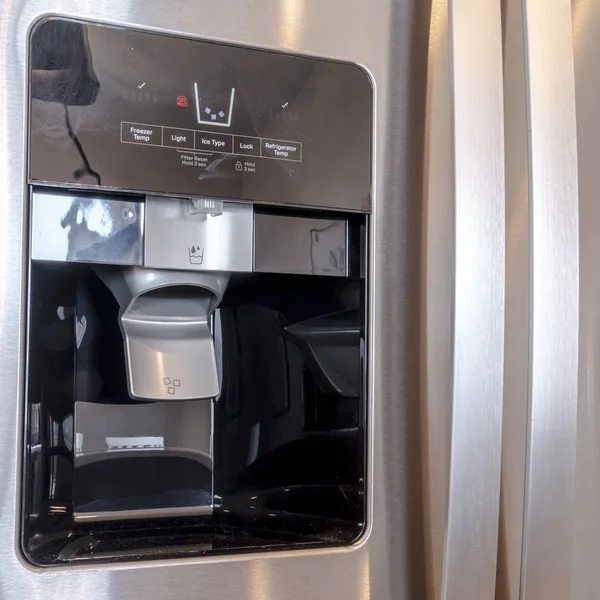 Square Water and ice dispenser on the shiny door of a refrigerator inside a home