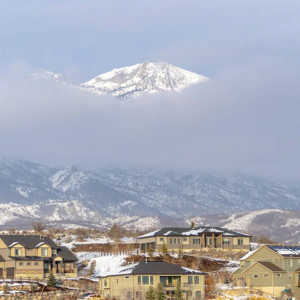 Photo Maisons carrées avec vue sur un sommet de montagne enneigé contre des nuages épais en hiver — Photo