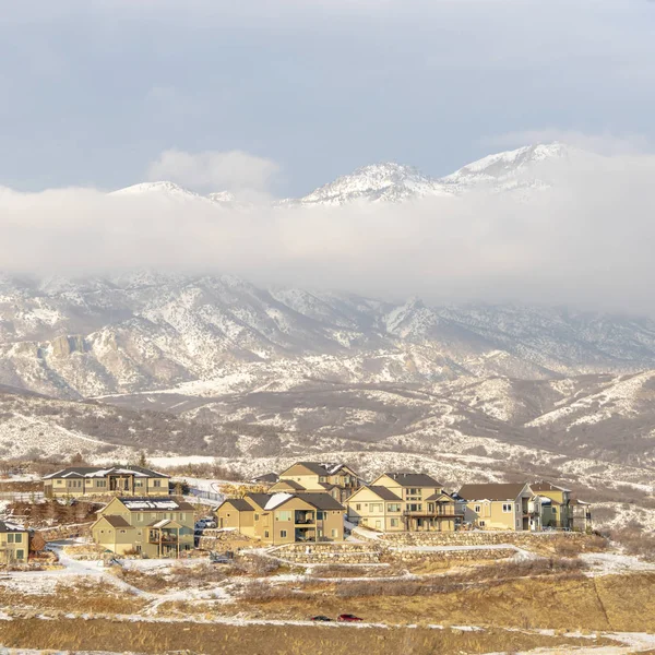 Foto Square Casas con vista a la montaña nevada parcialmente cubierta de nubes en invierno — Foto de Stock
