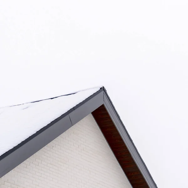 Square frame Home exterior with close up view of the gable roof covered with sheet of snow