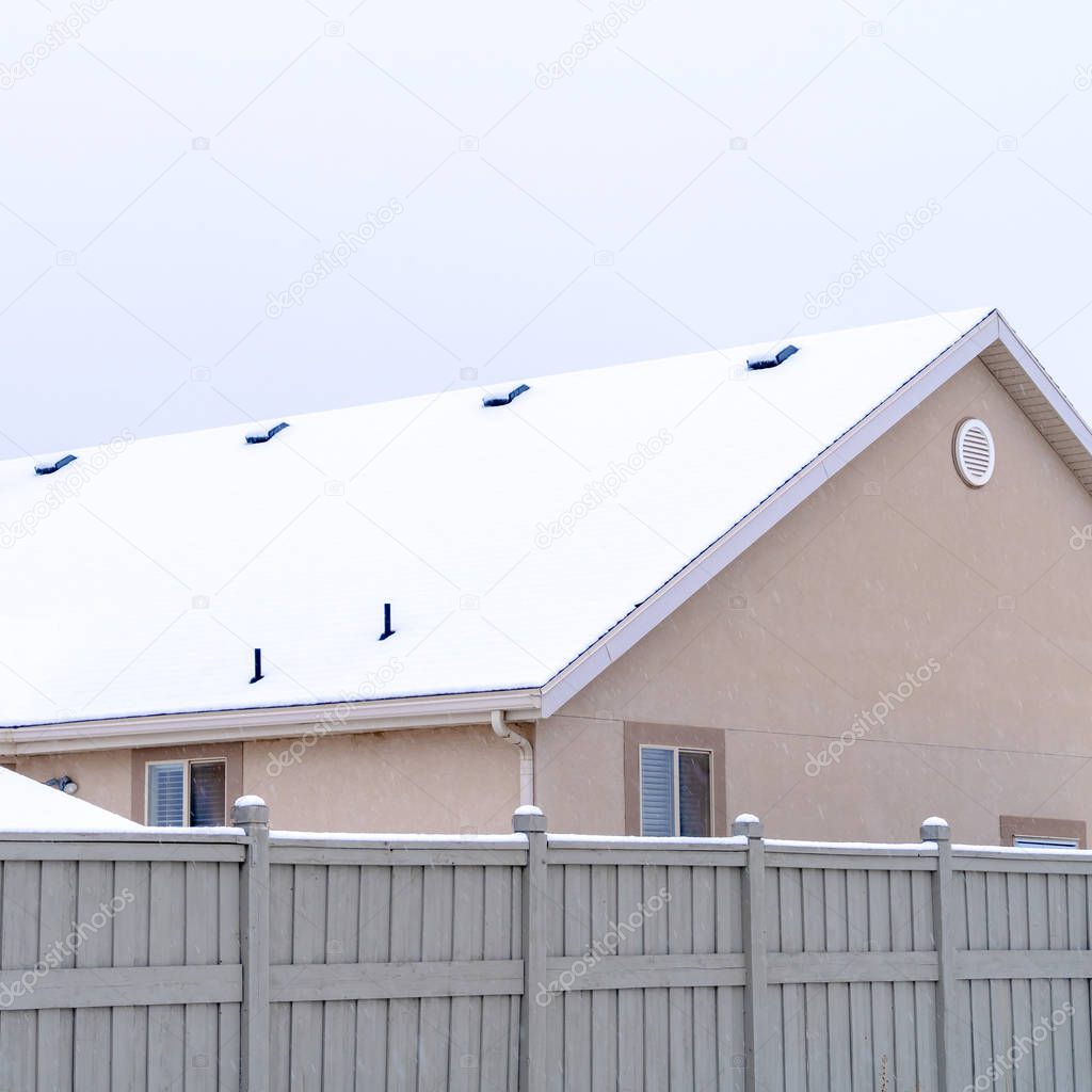 Square Home exterior with gable roof blanketed with snow against cloudy sky in winter